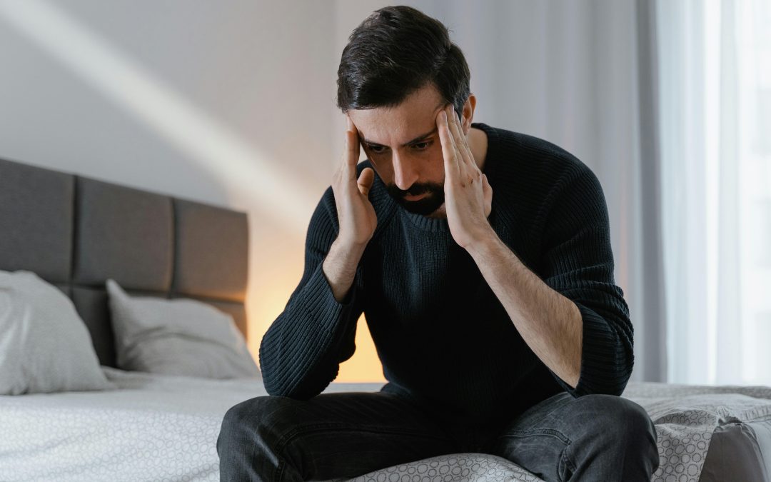 A man sitting on a bed rubbing his temples in distress.